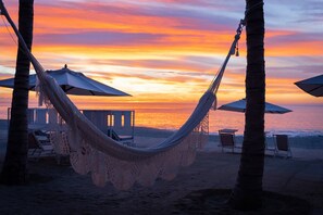 Eine Hängematte zwischen Palmen am Strand mit Blick auf den Sonnenuntergang.