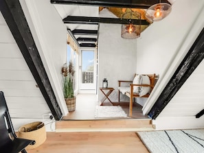 A narrow hallway with a wooden floor, a white door leading outside, a small table with a lantern, and a chair with a cushion. - "Arendine" - 250m from the sea by Interhome (Ørsted)