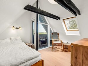 A bedroom with a bed, a chair, a small table, a wooden cabinet, a window with a view, and a door leading to an outdoor area. - "Arendine" - 250m from the sea by Interhome (Ørsted)