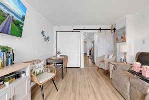 Ein modernes Wohnzimmer mit Holzboden, einer Couch, einem Essbereich mit Stühlen, einem Fernseher und einer Küche im Hintergrund.