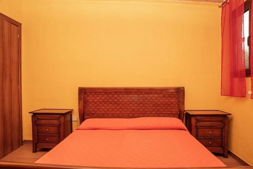 A room with a bed, two nightstands, a wooden headboard, and a red curtain.
