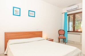 A bedroom with a wooden bed, a nightstand, a chair, and two framed pictures on the wall. - Résidence Villa Smeralda (Telti)