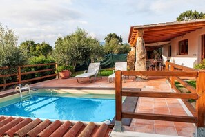 A swimming pool with lounge chairs, a wooden deck, and a stone pillar. - Résidence Villa Smeralda (Telti)