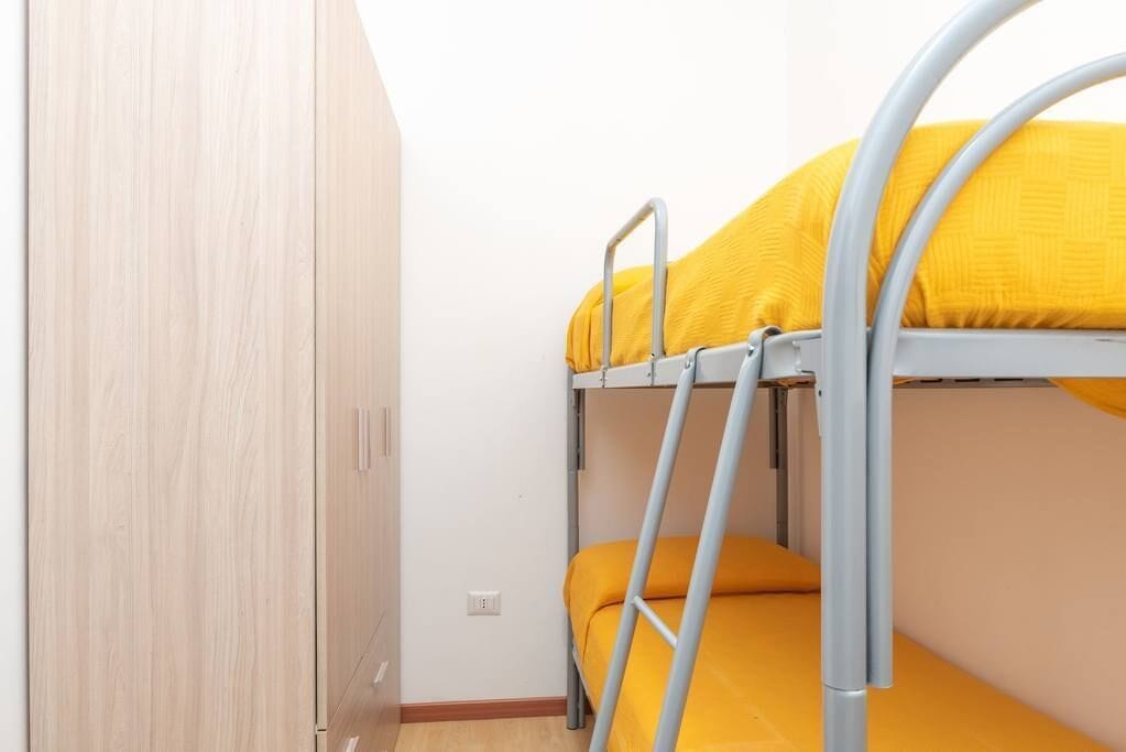 Una cama litera con ropa de cama amarilla, una escalera metálica y un armario de madera.