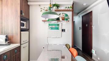 A compact kitchen with a microwave, a coffee machine, and a hanging green pendant light.