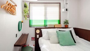 Une chambre à coucher comprenant un lit, une table de chevet, un porte-vêtements suspendu en bois, une fenêtre avec des stores, une plante en pot et une caméra fixée au mur.