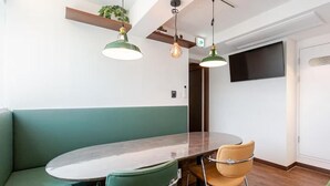 Un coin repas avec une table ronde, deux chaises, un banc vert et des luminaires suspendus.