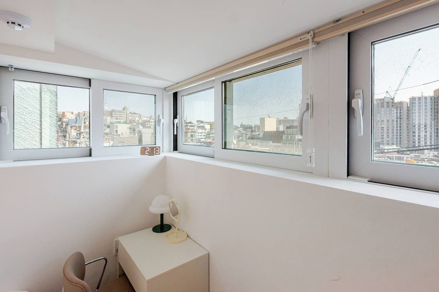 A room with a desk, chair, and three windows with views of buildings.