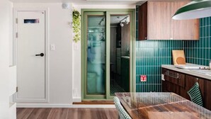 Une cuisine dotée d’un plan de travail en bois, d’un luminaire suspendu vert et d’une porte avec un panneau en verre dépoli.