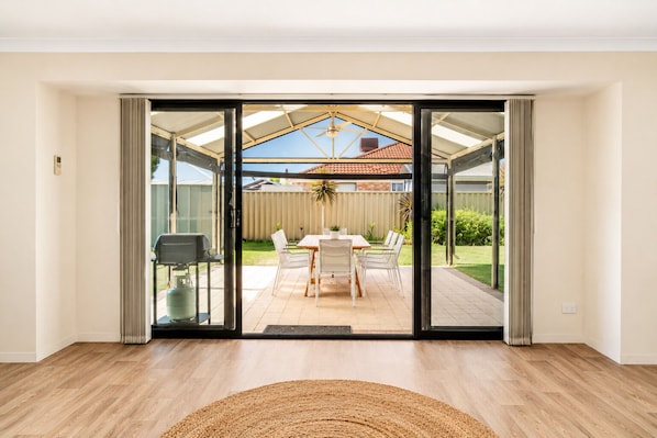 A modern room with a sliding glass door leading to an outdoor patio with a table and chairs. - Sandpiper House (Broadwater)