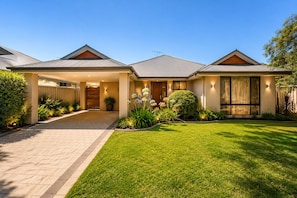 A modern two-story house with a covered driveway, a well-maintained lawn, and a variety of plants. - Sandpiper House (Broadwater)