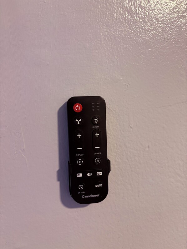 A black remote control with a red power button, directional buttons, and a mute button on a white wall.