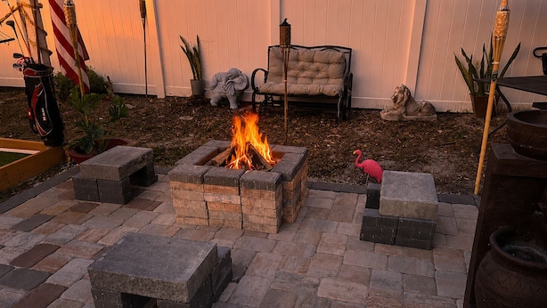 Un pozo de fuego rodeado de asientos de piedra, una silla de lounge y una estatua de flamenco.