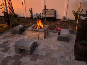 A fire pit surrounded by stone seating, a lounge chair, and a flamingo statue.