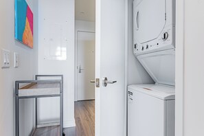 Ein Waschraum mit einer Waschmaschine, einem Wäscheständer und einem farbenfrohen, abstrakten Gemälde an der Wand.