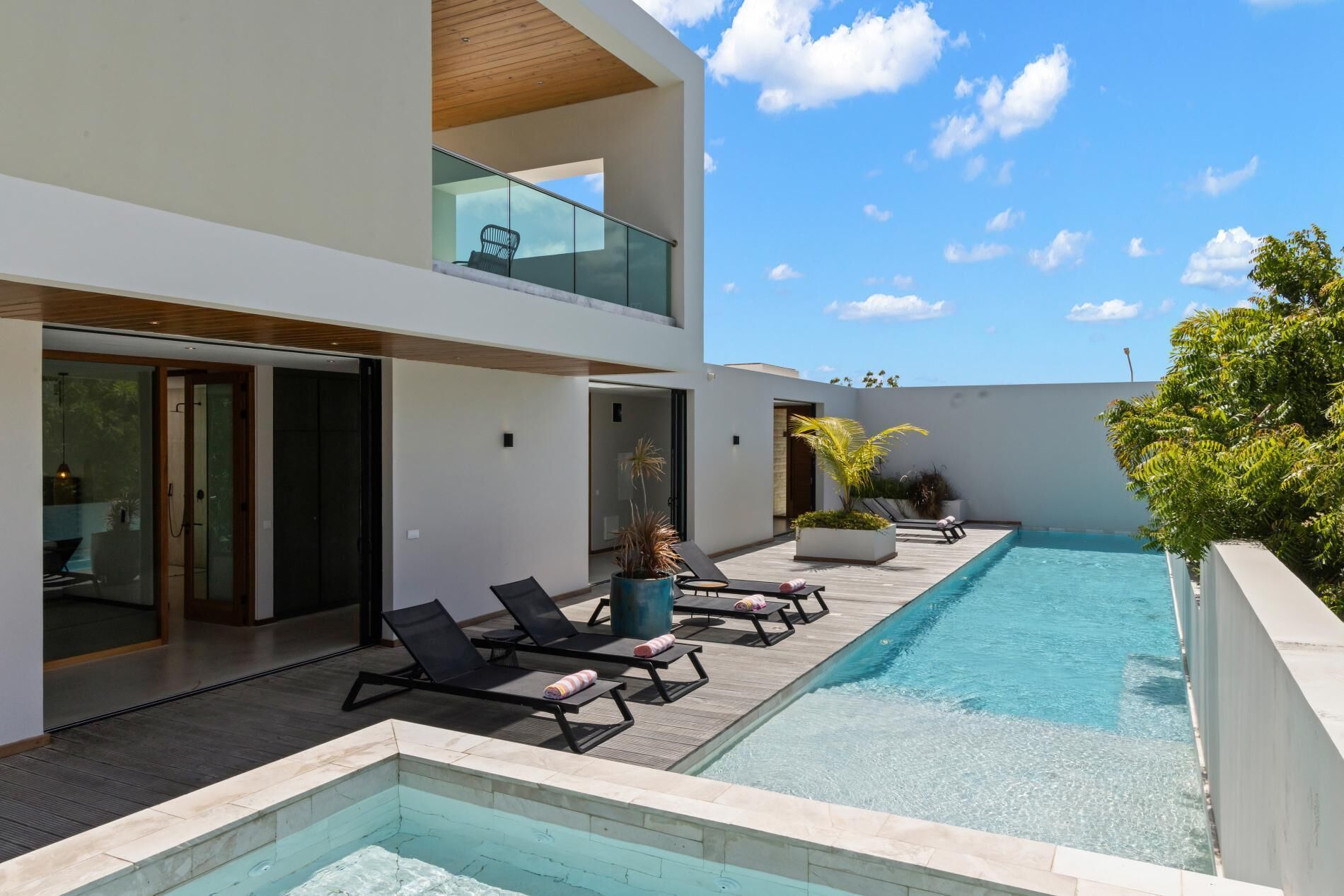 Un espace piscine extérieur moderne, doté de chaises longues et d’une balustrade en verre.