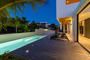 Un espace piscine extérieur moderne, doté d’une terrasse en bois, de chaises longues et offrant une vue sur le paysage environnant.