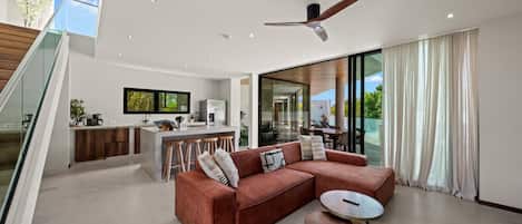 A modern living room with a sofa, a coffee table, and a dining area with a kitchen in the background.