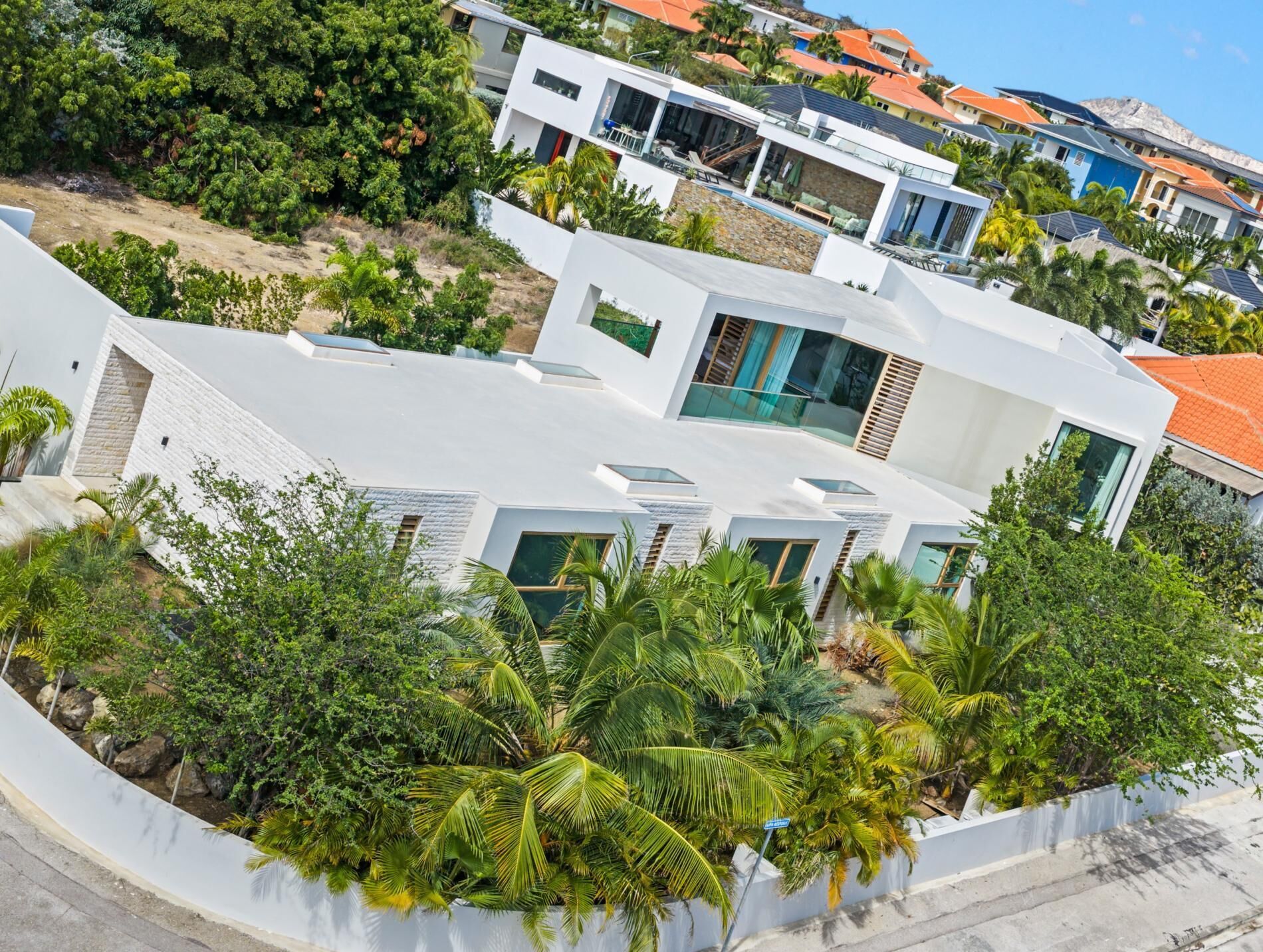 A modern residential building with multiple levels, surrounded by lush greenery and palm trees.