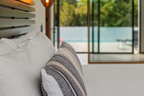 Een bed met gestreepte kussens en uitzicht op een zwembad door een glazen deur.