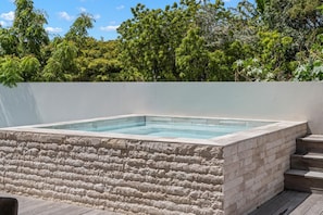 Ein rechteckiges Whirlpool mit Steinverkleidung, umgeben von einer weißen Mauer und einem Holzboden.