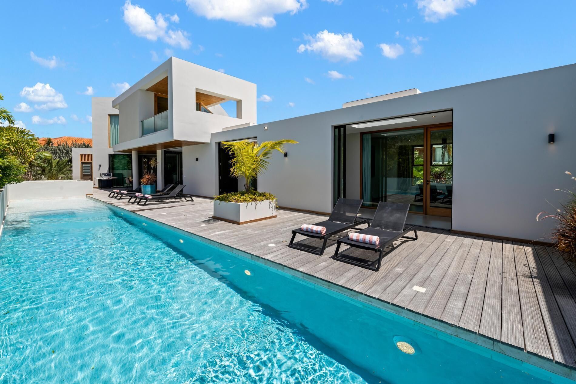 Ein moderner Poolbereich mit klarem, blauem Pool, Liegestühlen und einer Holzterrasse.