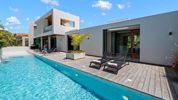 Ein moderner Poolbereich mit klarem, blauem Pool, Liegestühlen und einer Holzterrasse.
