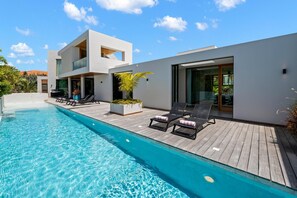 A modern poolside area with a clear blue pool, lounge chairs, and a wooden deck.