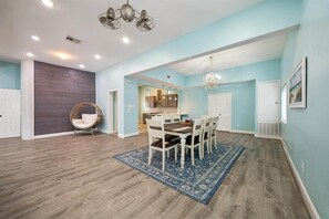 A spacious dining area with a wooden table, chairs, and a blue rug. - 1876 Historic Home • 2 Kitchens • Sleeps 10 • Cruise-Ready • (Galveston)