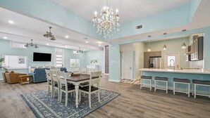 A spacious living room with a dining area, a kitchen with bar stools, and a large chandelier. - 1876 Historic Home • 2 Kitchens • Sleeps 10 • Cruise-Ready • (Galveston)