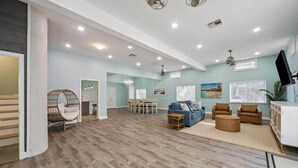 A spacious living area with a dining set, a blue sofa, and a television. - 1876 Historic Home • 2 Kitchens • Sleeps 10 • Cruise-Ready • (Galveston)