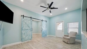 A room with light blue walls, a ceiling fan, a door, and a window with blinds. - 1876 Historic Home • 2 Kitchens • Sleeps 10 • Cruise-Ready • (Galveston)