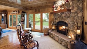 A cozy interior with a stone fireplace, wooden ceiling, and a bookshelf.
