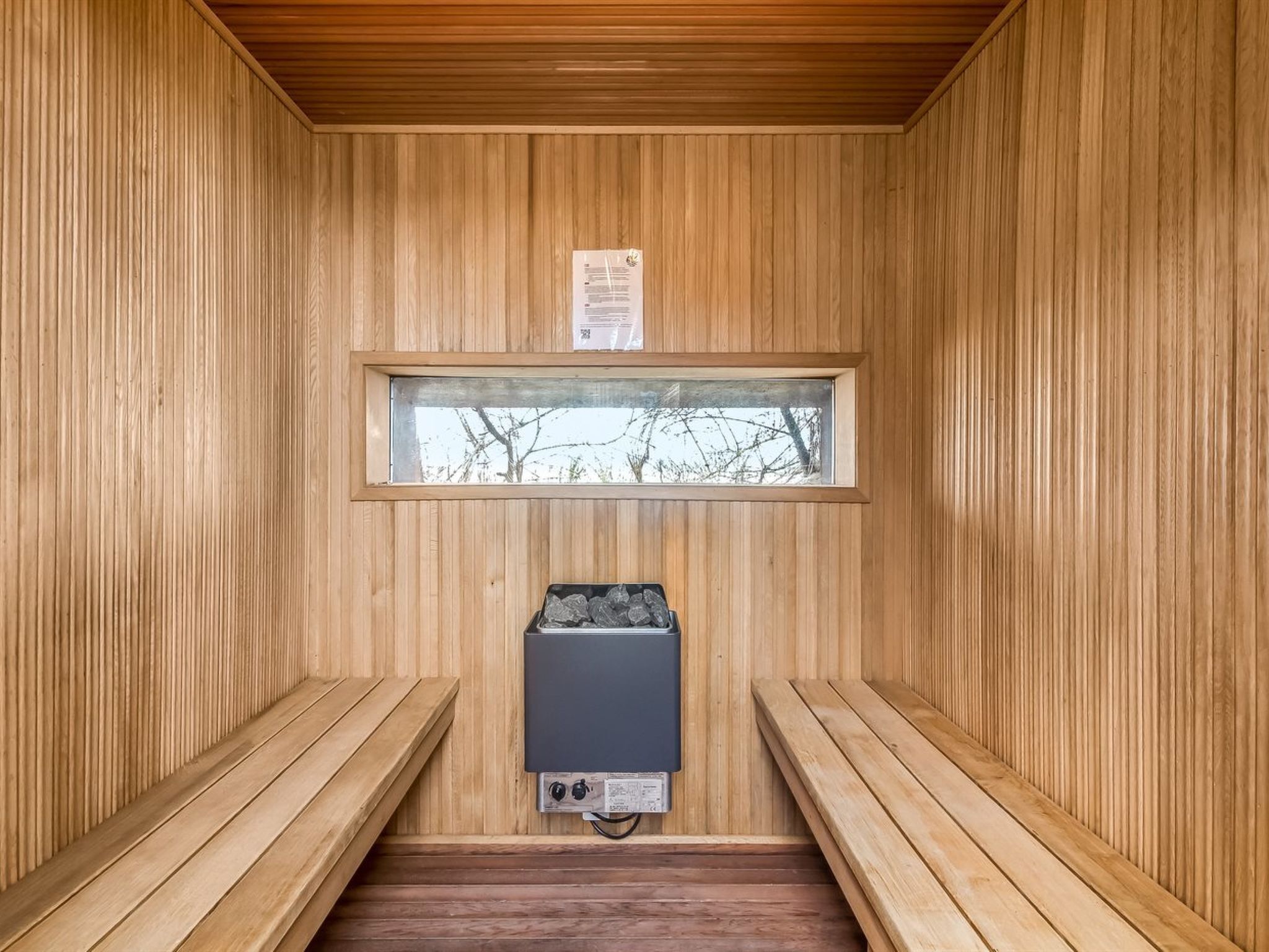 A sauna room with wooden walls, a window, and a sauna heater.