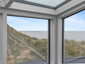 Ein Zimmer mit großen Fenstern mit Blick auf einen Strand und Dünen.