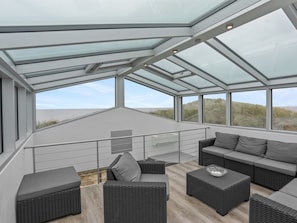 Eine moderne Außenterrasse mit Korbmöbeln, Glasüberdachung und Blick auf den Strand.