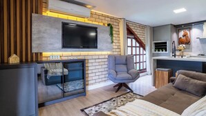 Ein modernes Wohnzimmer mit Fernseher, Sitzgelegenheiten und einer Küchenzeile.