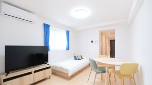 A modern room with a bed, a TV, a dining table with chairs, and an air conditioning unit. - Sees Kinshicho II (Tokyo)