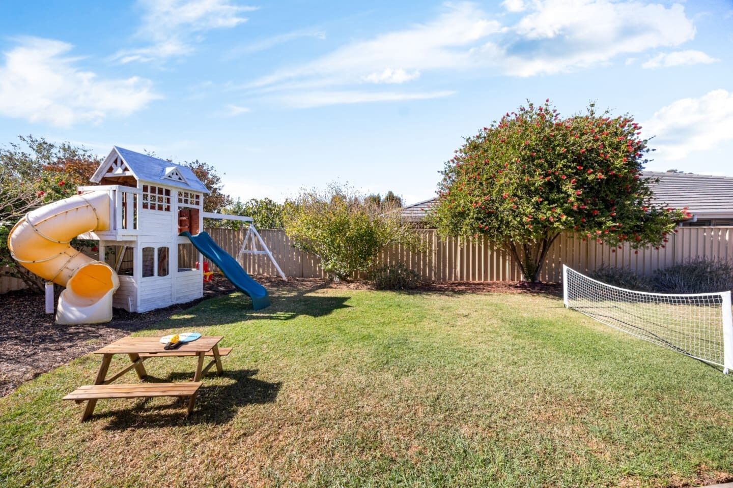 A backyard with a playhouse, a slide, a picnic table, and a tree.
