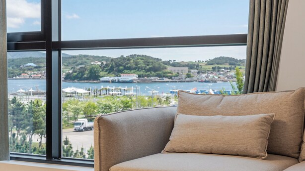 Una habitación con un amplio ventanal que ofrece vistas a un puerto deportivo, barcos y un paisaje montañoso.