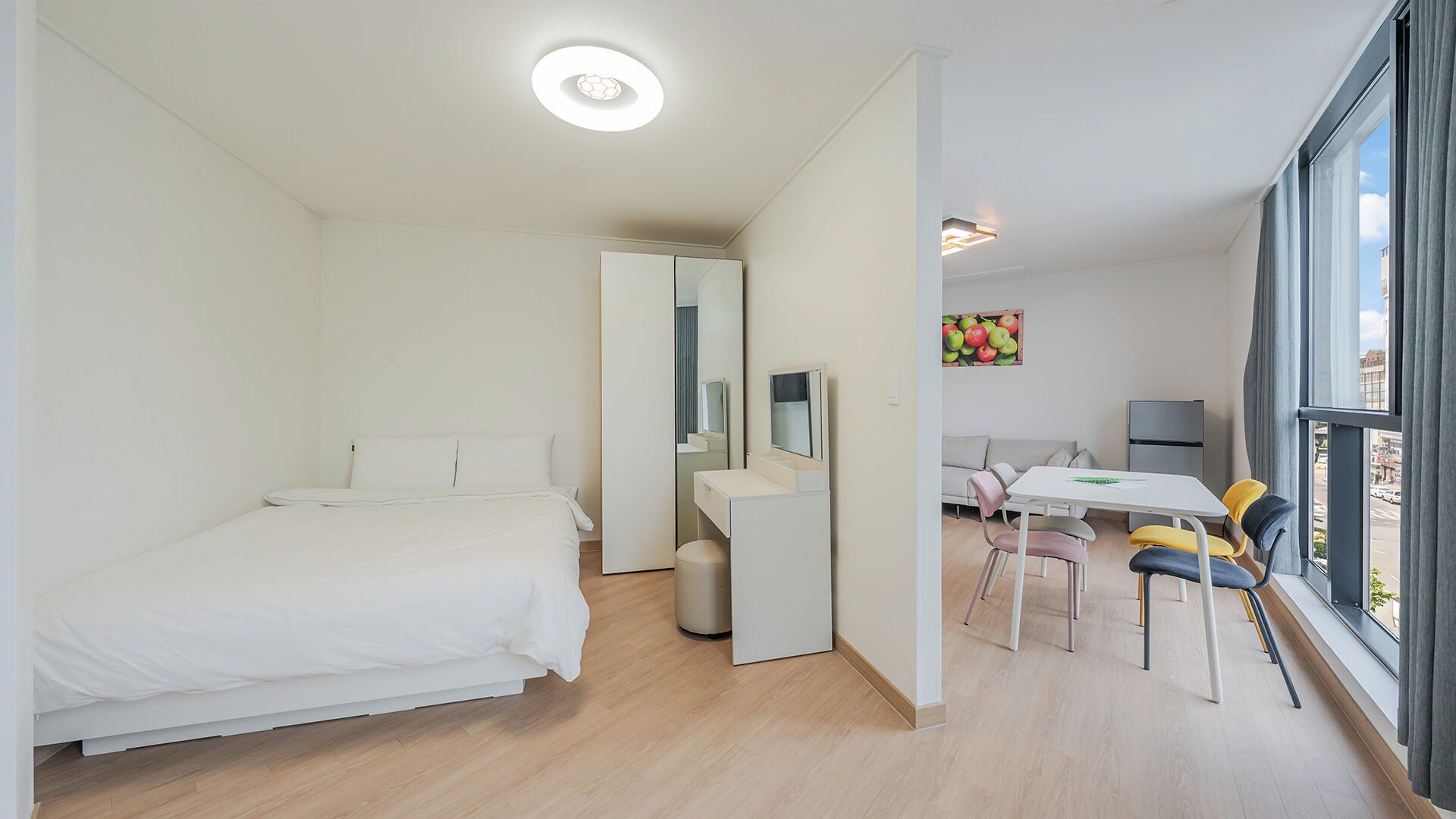 A modern hotel room with a bed, a desk, a chair, a mirror, and a window.