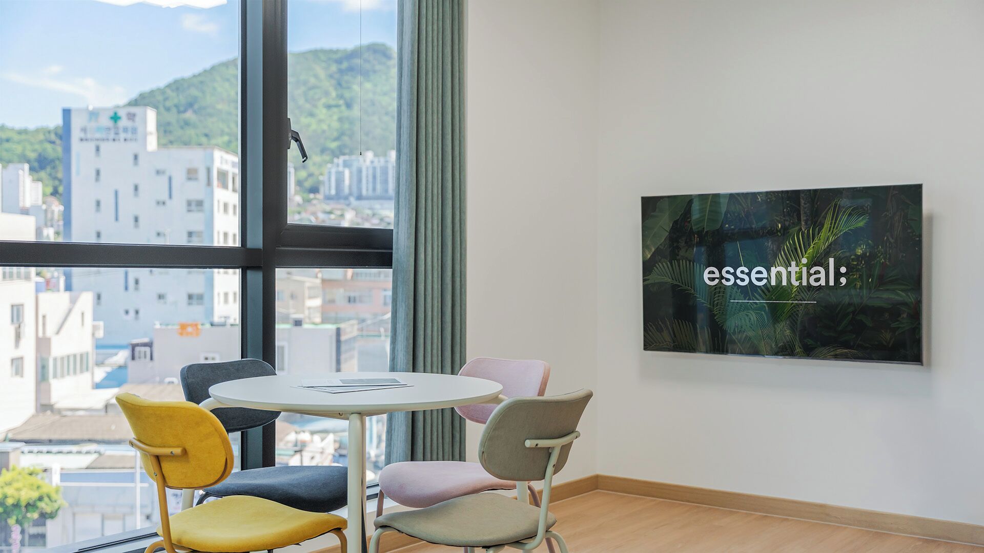A room with a round table, four chairs, a window with a city view, and a framed picture on the wall.