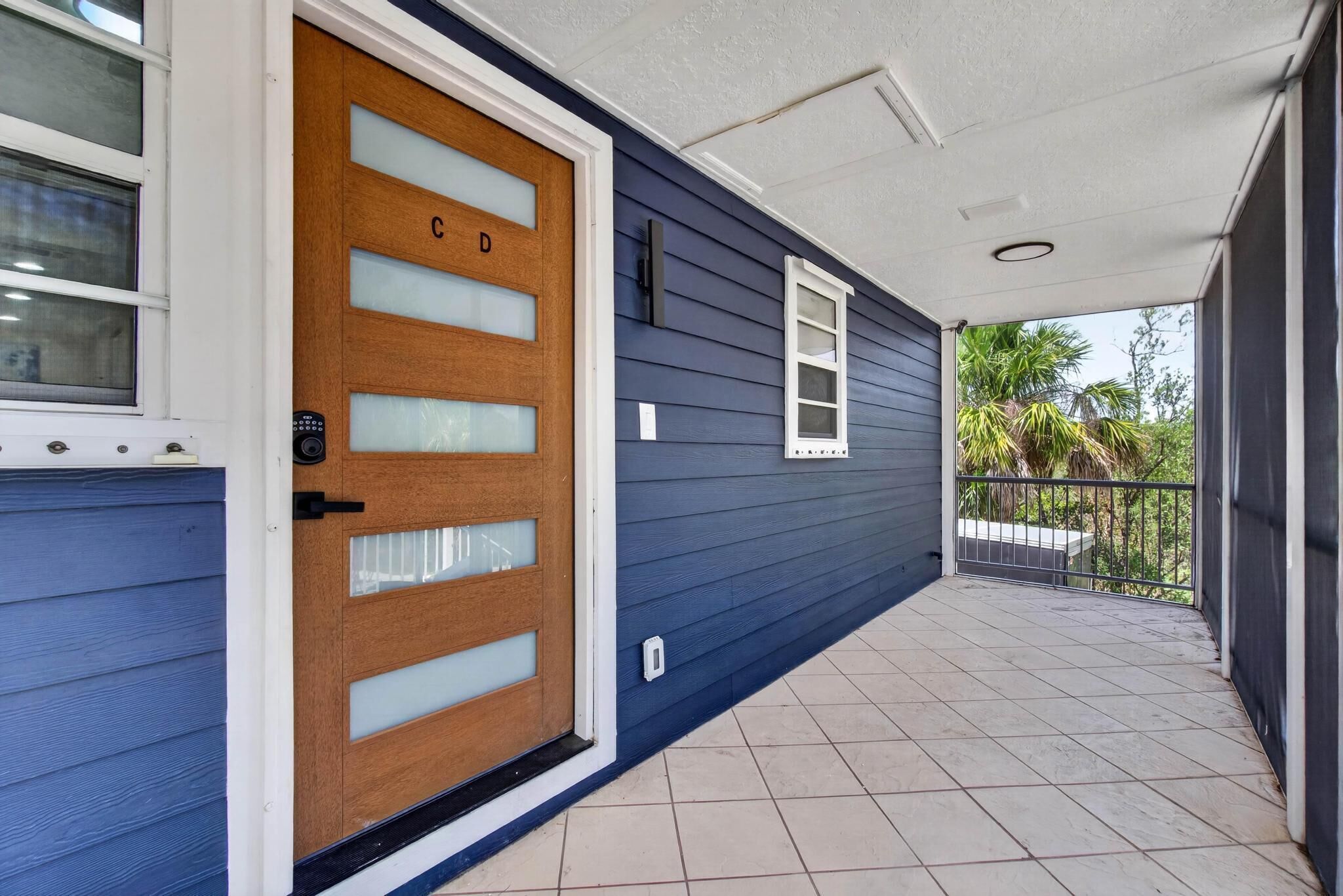 Una casa con facciata blu, una porta d'ingresso in legno con vetri decorati e un piccolo finestrino, e un portico piastrellato.