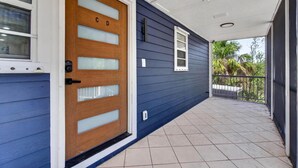 A house with a blue exterior, a wooden front door with frosted glass panels, a small window, and a tiled porch. - Spacious Waterfront Home_Sleeps 16_7BR_Spacious (Palmetto)