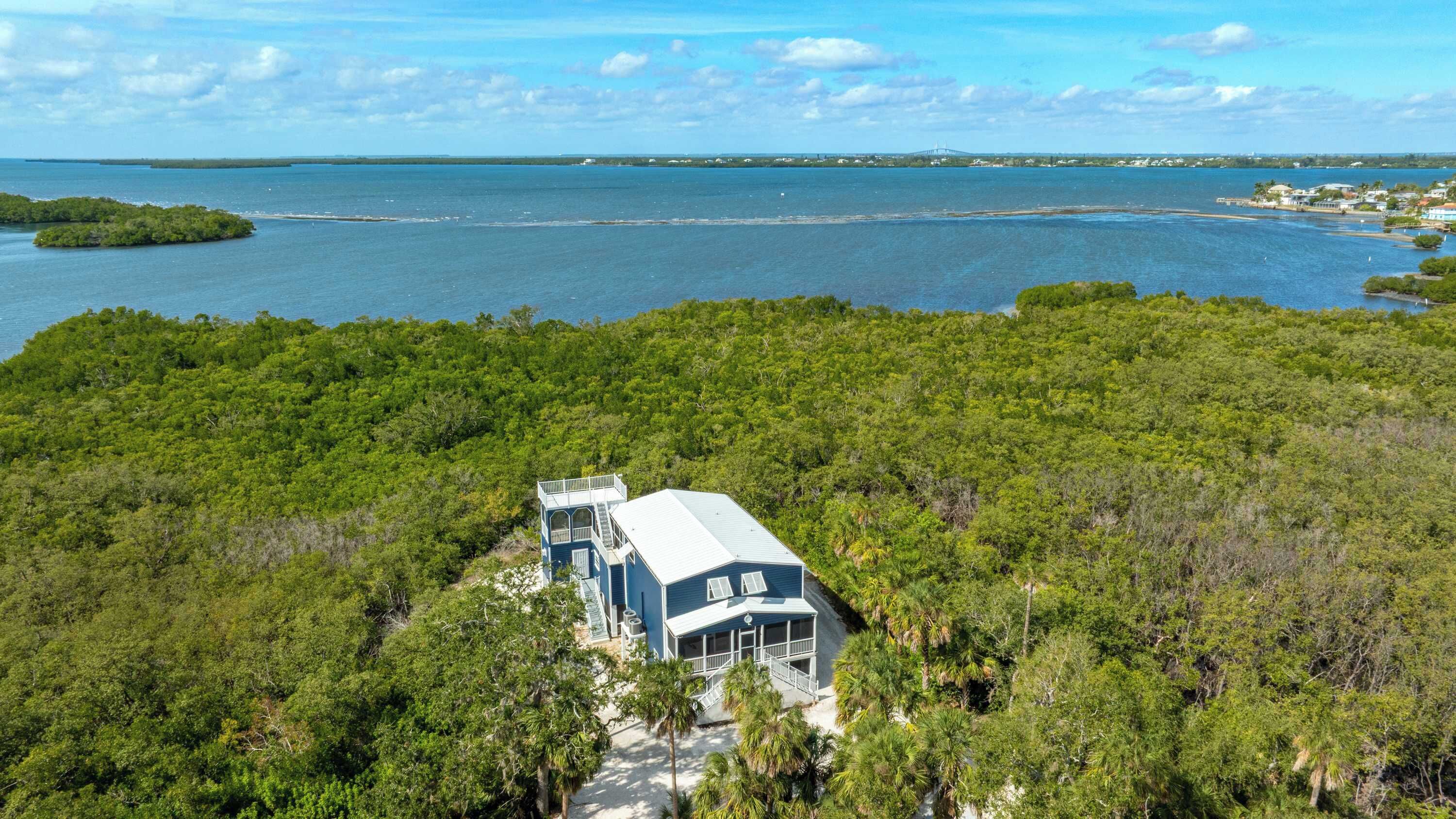 A coastal property with a large house surrounded by dense forest, a view of the sea, and a distant bridge.