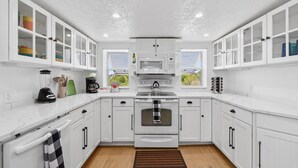 A modern kitchen with white cabinets, a built-in oven, a microwave, and a window with blinds. - Spacious Waterfront Home_Sleeps 16_7BR_Spacious (Palmetto)