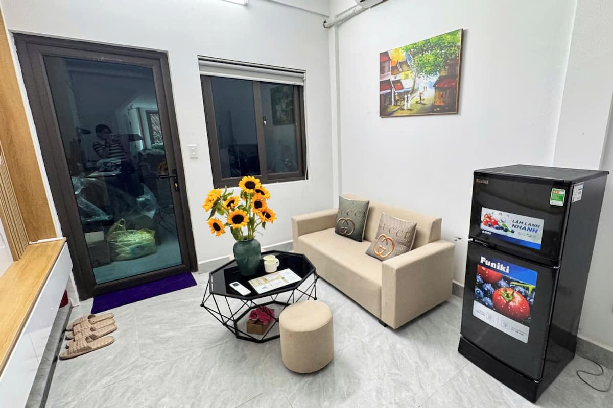 A modern room with a sofa, a coffee table with a vase of sunflowers, a refrigerator with a Funiki advertisement, and a painting on the wall.