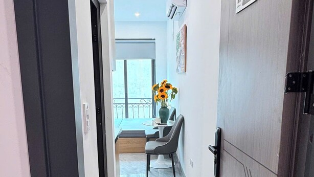 Um corredor com uma porta identificada como '501', uma pequena mesa com um vaso de girassóis e vista para uma varanda.