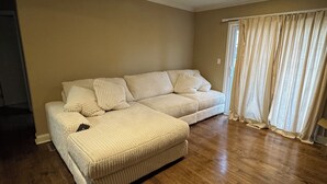 A beige-colored sofa with striped cushions in a room with wooden flooring and a window with curtains. - Quiet West Plaza Retreat – Spacious Condo in Prime KC Location. (Kansas City)