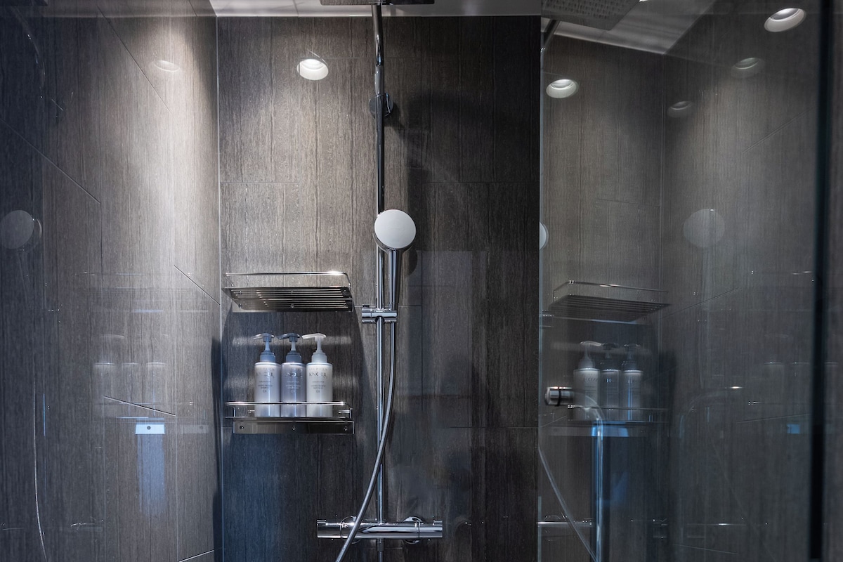 A modern shower with a glass enclosure, a handheld showerhead, and a towel rack.